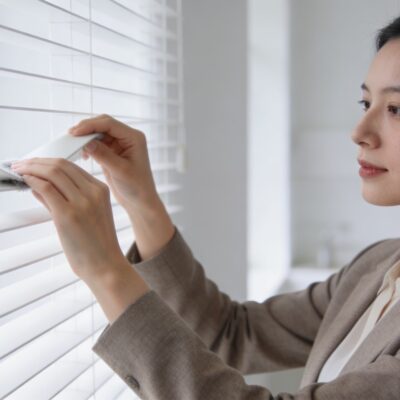 Femme debout nettoyant des stores vénitiens blancs dans un salon lumineux