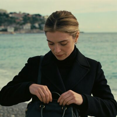 Femme debout sur plage de Nice ajustant sac devant mer