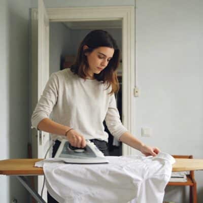 Jeune femme repassant chemise blanche dans petit appartement parisien lumineux