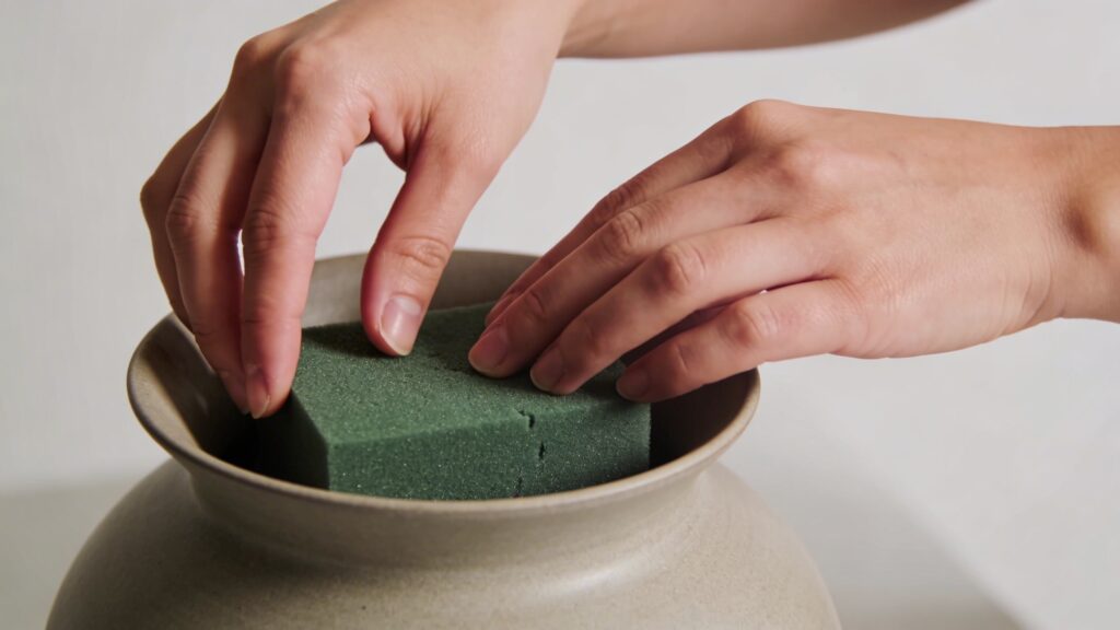 Mains ajustant bloc de mousse verte dans vase