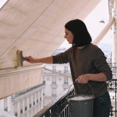Personne nettoyant un store banne beige sur balcon parisien ensoleille